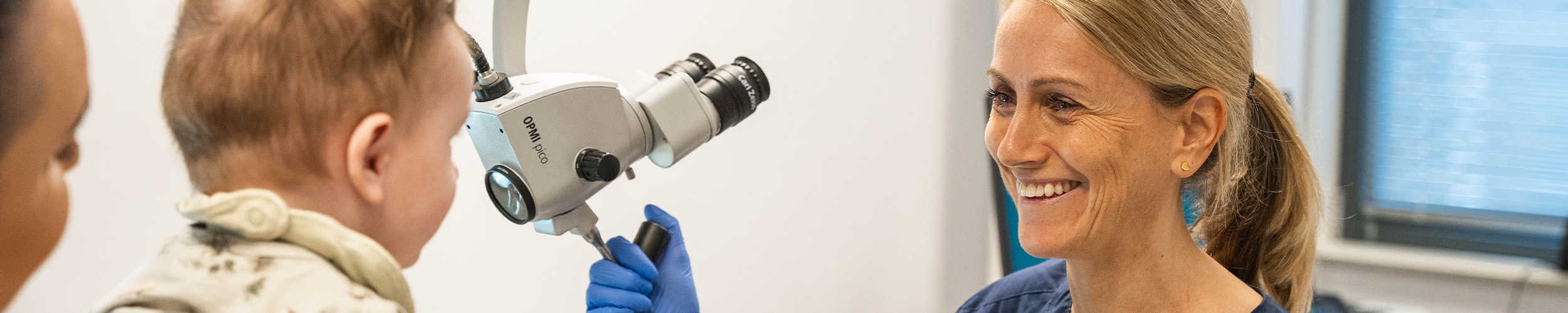 ØNH-spesialist Ingvild Nesse Østerhus smiler til et lite barn som sitter på morens fang. 