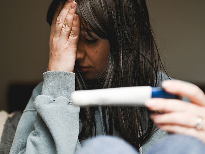 trist kvinne med graviditetstest i sofaen.