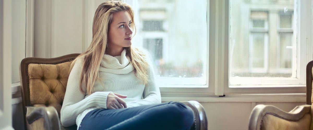 Ung kvinne som sitter og tenker på noe mens hun ser ut av et vindu. 