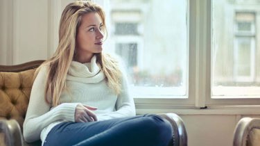 Ung kvinne som sitter og tenker på noe mens hun ser ut av et vindu.