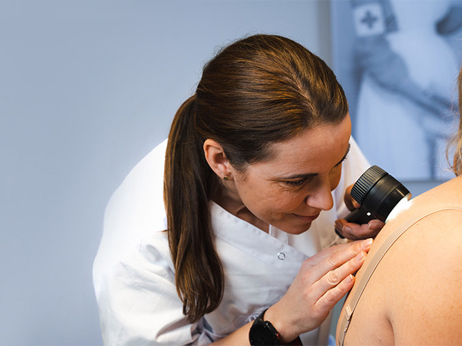 Hudlege sjekker en føflekk på pasient.