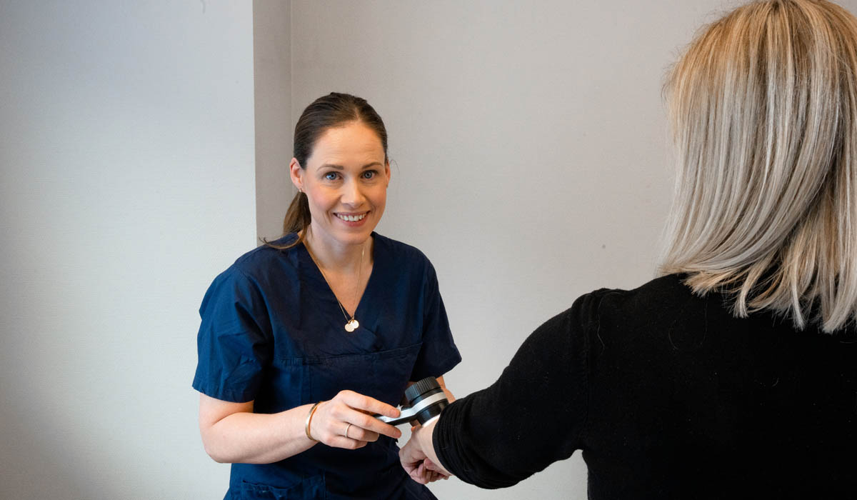 Hudlege Silje Davik undersøker en kvinnelig pasients hånd. 