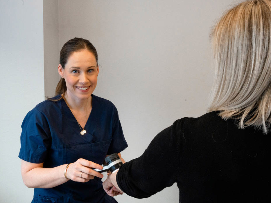 Hudlege Silje Davik undersøker en kvinnelig pasients hånd.