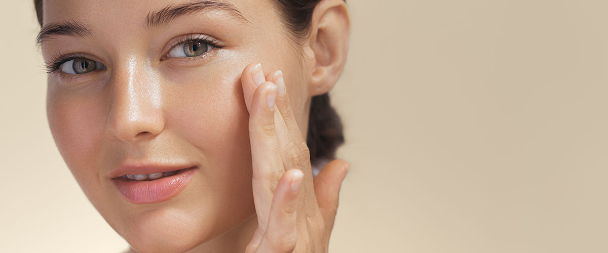 Ung kvinne med vakker hud påfører hudprodukt.