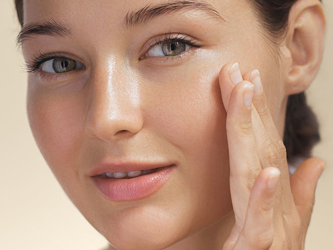 Ung kvinne med vakker hud påfører hudprodukt.