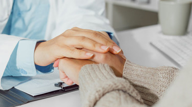 lege som holder hånden sin over hånden til en pasient. 