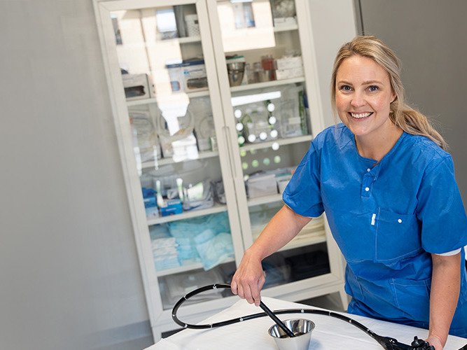 Kvinne som smiler og holder et skop inne på et behandlinsrom.