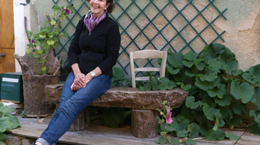 Kvinne sitter utenfor huset sitt med grønne planter