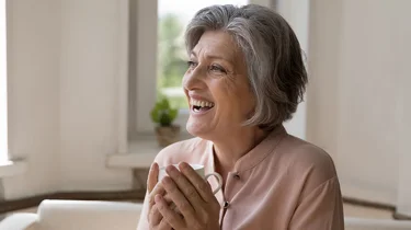 fornøyd dame 60 år sitter i sofaen.