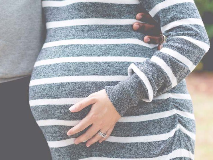 gravid kvinne holder seg på magen.