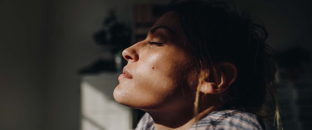 kvinne som får litt lys på ansiktet i et ellers mørkt rom. 